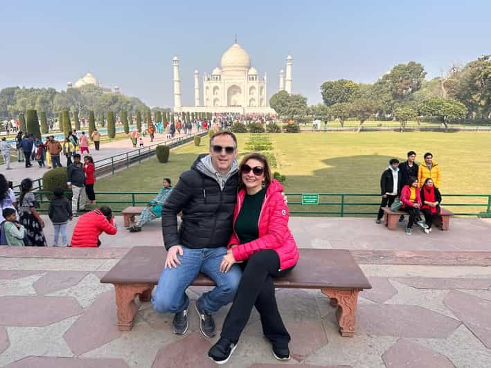Couple sitting together on a bench posing in front of the Taj Mahal during a sunrise Taj Mahal tour