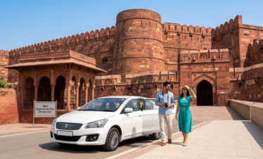 A white private tour car parked in front of the massive red sandstone walls and fortified entrance of Agra Fort. A couple is seen walking toward the monument, capturing the scale of this UNESCO World Heritage site.