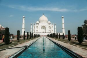 "The Taj Mahal in Agra, India, with its white marble dome and four minarets reflected in the long central water channel, surrounded by manicured gardens under a clear blue sky