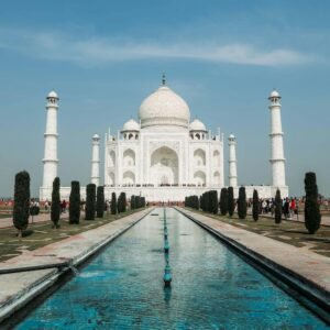 "The Taj Mahal in Agra, India, with its white marble dome and four minarets reflected in the long central water channel, surrounded by manicured gardens under a clear blue sky