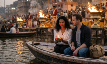 A couple sitting on a traditional wooden boat in Varanasi during the evening. The woman holds a small, lit flower lamp (diya) as they watch the glowing fire ceremonies and crowds at the ghats from the water.