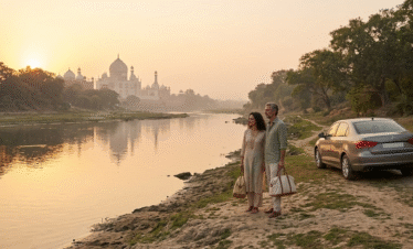 A man and woman standing on the sandy banks of the Yamuna River, peacefully viewing the Taj Mahal in the distance during a hazy sunrise. A silver car is parked on a nearby dirt path, emphasizing a private, off-the-beaten-path moment.