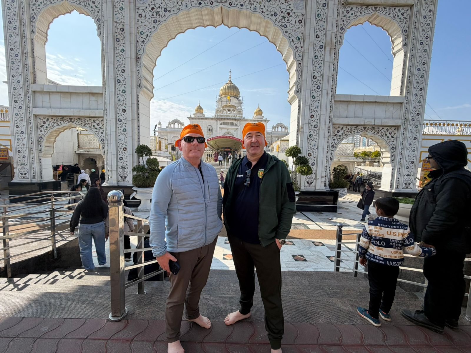 Visitors standing barefoot at the ornate entrance of a Sikh Gurdwara with golden domes, wearing traditional orange head coverings – highlighting North India’s cultural and religious tourism.