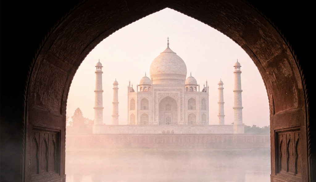 Taj Mahal sunrise tour view through a Mughal archway with morning mist over Yamuna River.