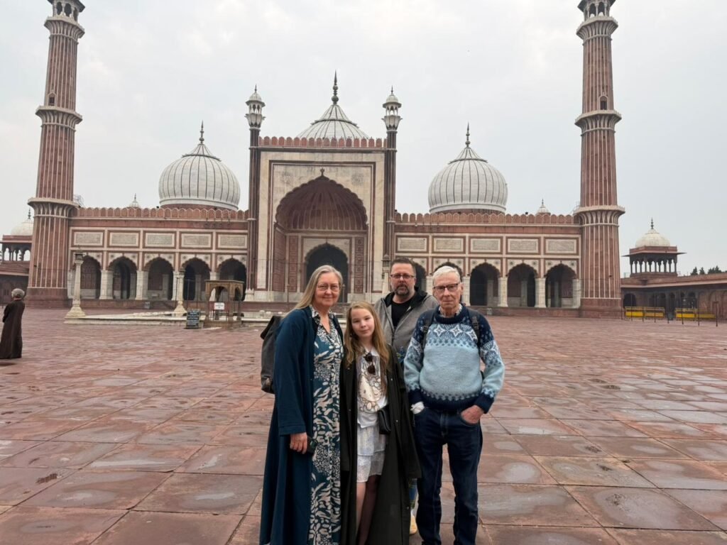 Tourists posing in front of Jama Masjid Delhi, showcasing Mughal architecture with domes, minarets, and expansive red sandstone courtyard – a major North India sightseeing attraction.